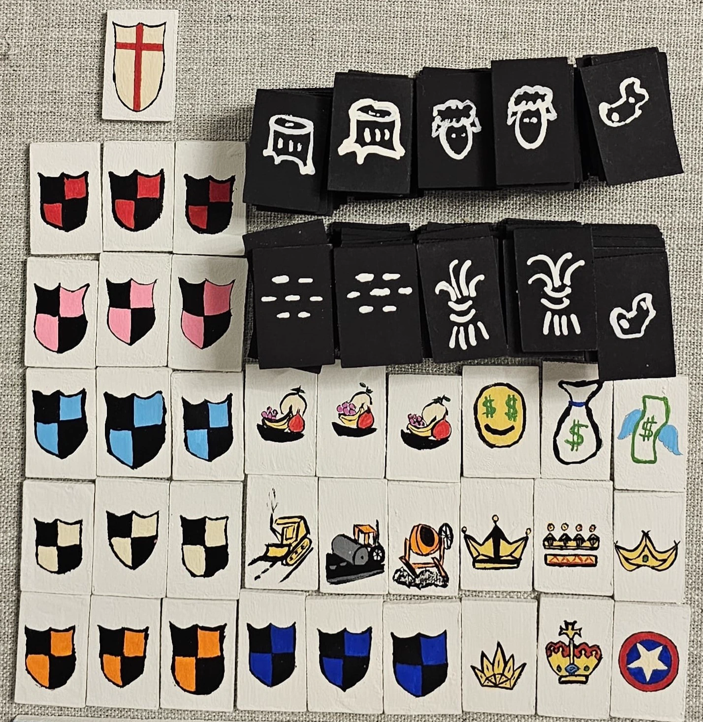 A collection of hand-painted wooden game tiles decorated with shields, crowns, and other small symbols.